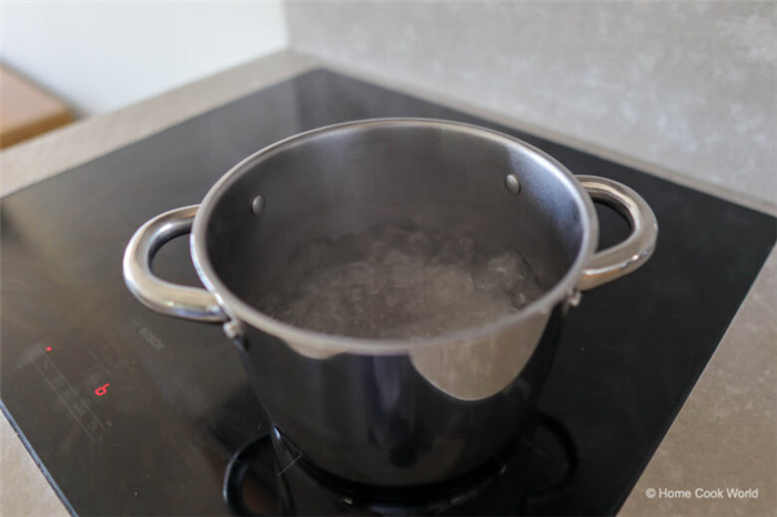 Фотография кастрюли из нержавеющей стали с кипящей водой на индукционной плите.